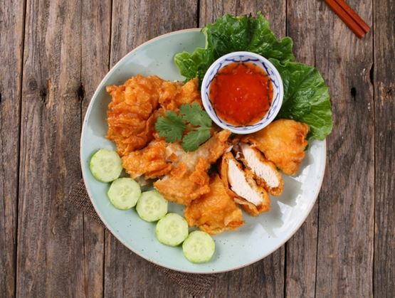 Poulet frit croustillant accompagné de sauce aigre-douce, servi avec des rondelles de concombre sur une assiette.