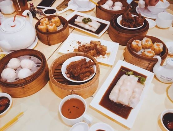 Restaurant table featuring an assortment of dim sum served in bamboo steamers, including buns, rice rolls, dumplings and sauced dishes, accompanied by tea and dipping sauces.
