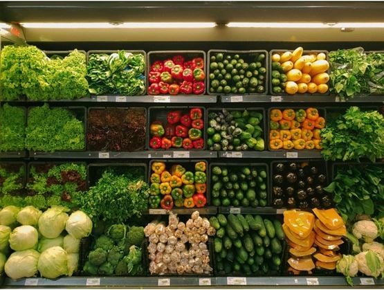 Display of fresh vegetables in a supermarket, with neatly arranged rows of lettuce, peppers, cucumbers, zucchinis, eggplants, and other green and colorful produce.
