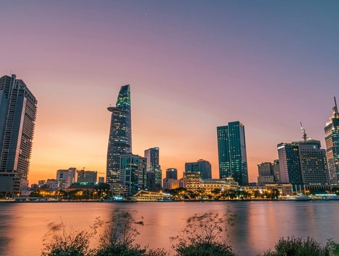 Panoramic view of the Ho Chi Minh City skyline at sunset, with modern skyscrapers reflecting on the river.