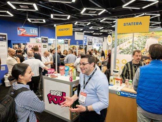 Visitors and exhibitors talk around food stands at a busy trade show.