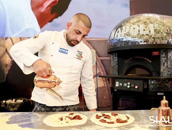 Chef preparing pizzas at a SIAL trade show booth in China, next to a professional pizza oven.