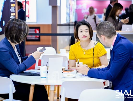 Three professionals talk around a table at a SIAL trade show in China, in a business meeting area.