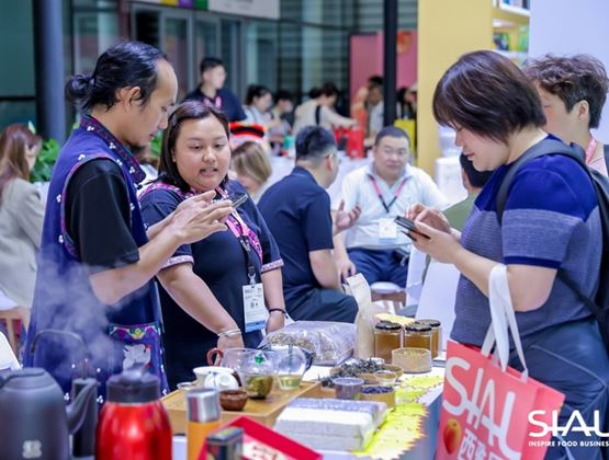 Visitors discovering products and beverages at a SIAL trade show booth in China, with exhibitors presenting their offerings.