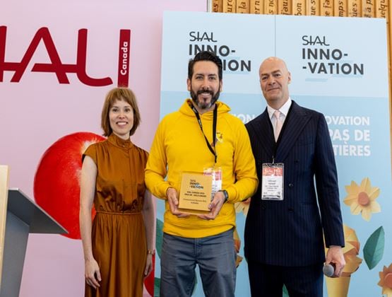 Three people at SIAL Innovation Canada, with the Kunana representative in a yellow hoodie holding the Gold Award for banana milk.