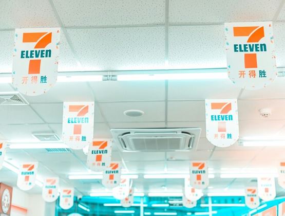 7-Eleven signs hanging from the ceiling inside a brightly lit convenience store.