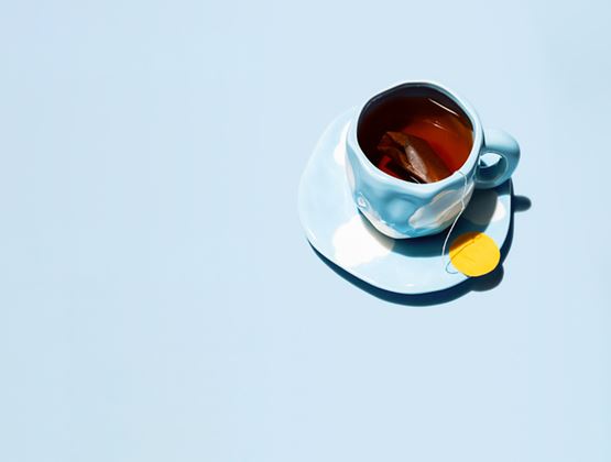Tasse de thé sur soucoupe bleu clair avec sachet infusé et étiquette jaune, sur fond bleu pastel.