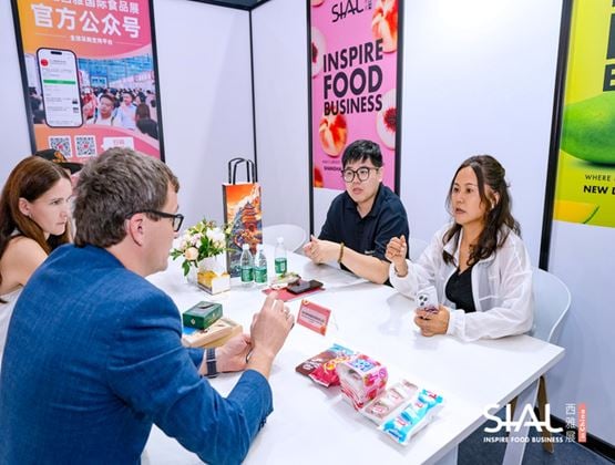 Business meeting between exhibitors and buyers at a SIAL trade show booth, with product samples displayed on the table.