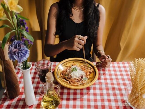 Woman eating a plate of spaghetti at a table covered with a red-and-white checked tablecloth.