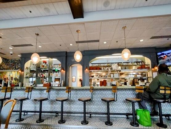 Restaurant interior with a long tiled bar, high stools and an open kitchen in the background.