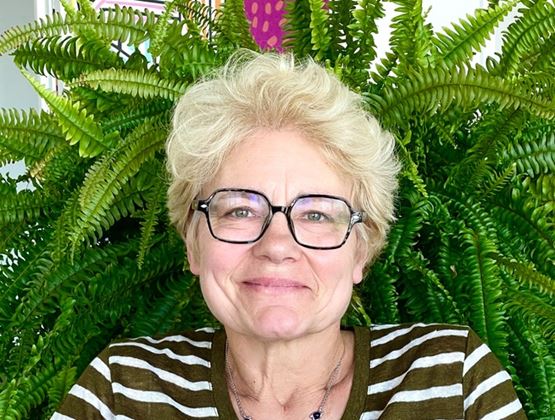 Portrait of Sophie de Reynal wearing glasses, seated in front of lush green ferns.