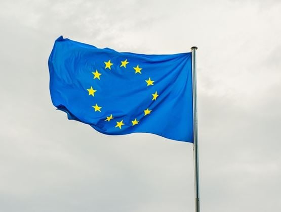 European Union flag waving on a flagpole against a cloudy sky.