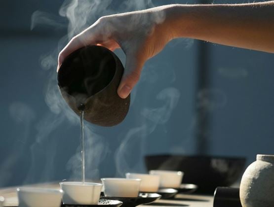 Steaming hot tea poured from a dark clay pot into small white cups during a traditional Chinese tea ceremony