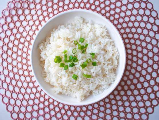 Bowl of white rice topped with chopped green onions, viewed from above.