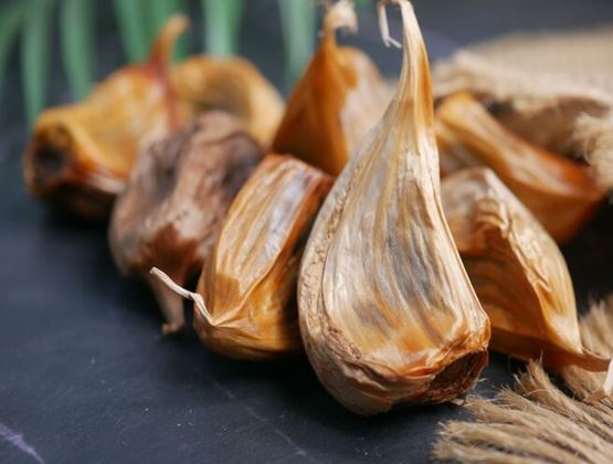 Close-up of black garlic cloves with caramel-brown skins on a dark slate surface, the key ingredient in La terre du 9’s product range.