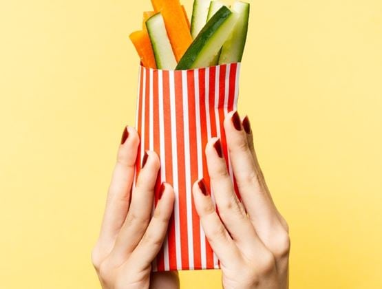 Hands holding a striped paper container filled with carrot and cucumber sticks