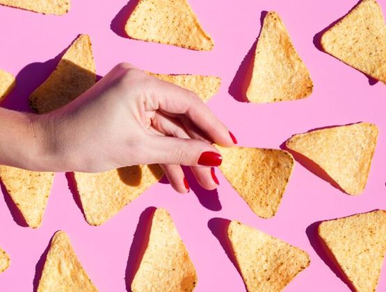 Hand taking a dorito chip with dorito chips on a pink background