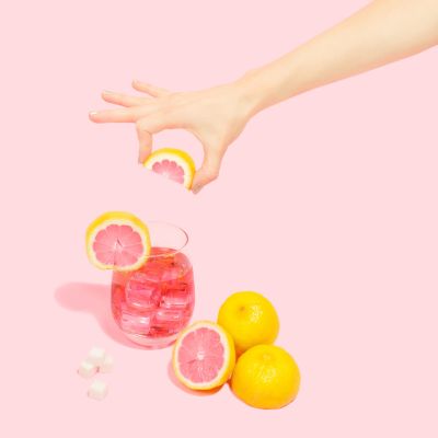 Glass of pink beverage with straw on a light pink background, minimalist composition.
