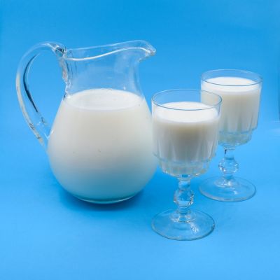 Milk jug and glasses arranged on a blue background, clean and minimal setup.