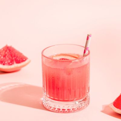Pink drink with ice cubes and grapefruit slice on a pastel pink background.