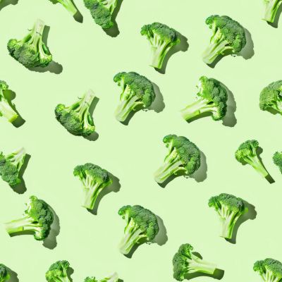 Broccoli florets arranged in a repeating pattern on a light green background.