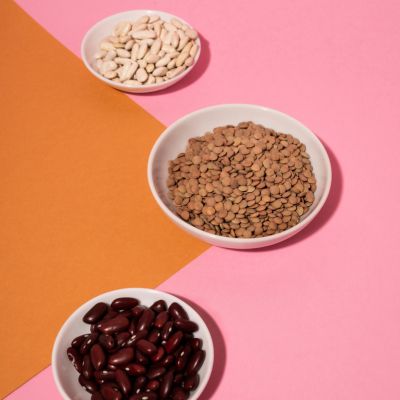 Assortment of legumes in white bowls on a pink and orange background.