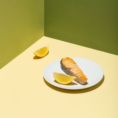 Grilled salmon fillet on a white plate with lemon wedge, green and yellow background.