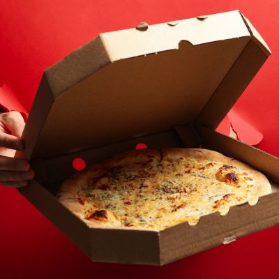 Cheese pizza inside an open cardboard box on a red background, minimalist food styling.