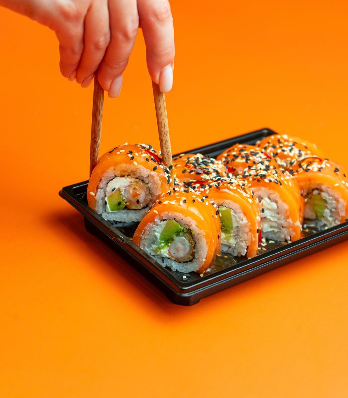 Tray of salmon sushi with chopsticks on a bright orange background.