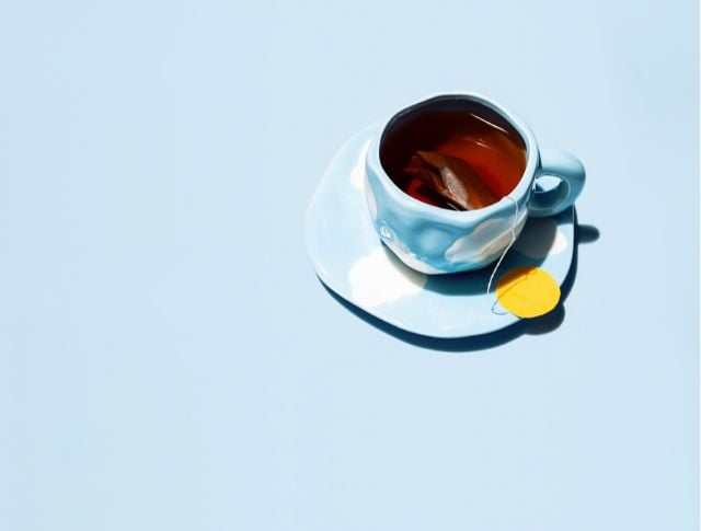 Blue cup with cloud patterns on a saucer, filled with tea and a yellow-tagged teabag.