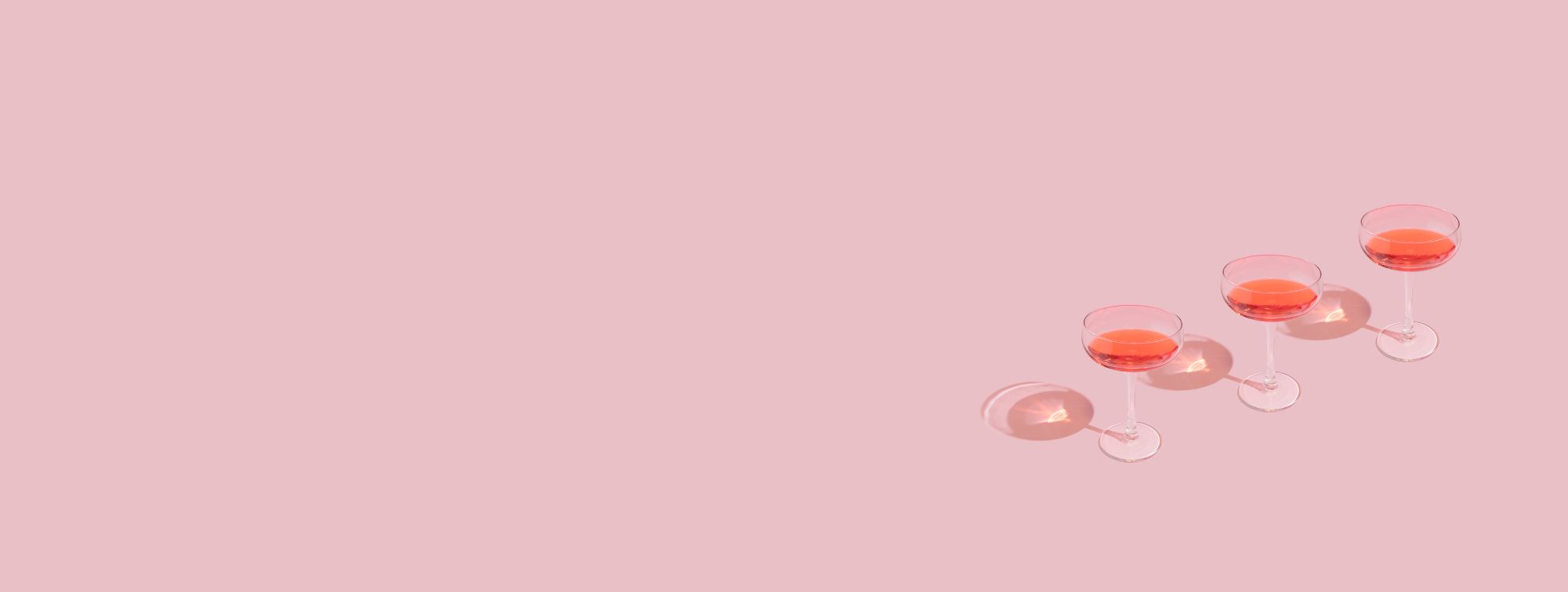 Three stem glasses filled with pink liquid, aligned on a pastel pink background.