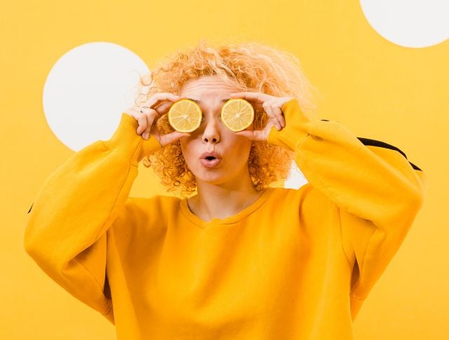 Person holding lemon slices over eyes on a yellow background illustrating a creative food trend