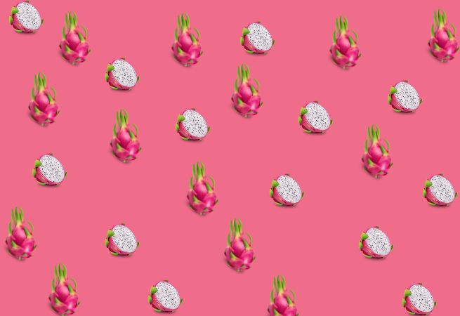 Pattern of whole and sliced dragon fruits on a pink background illustrating an exotic Asian fruit and food trend