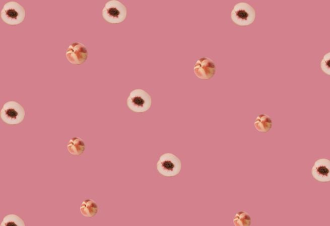 Pattern of whole and sliced peaches on a pastel pink background representing a trendy fruit universe