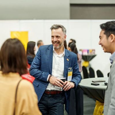 Professionals networking at a food industry B2B event, smiling man in blue blazer talking with two attendees.