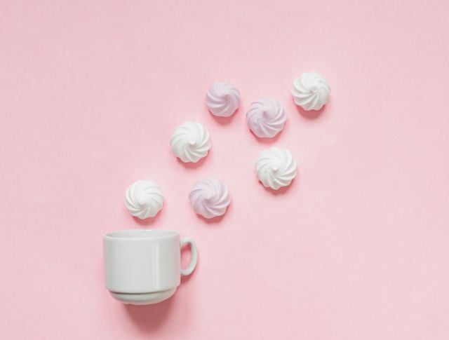 White cup with meringues arranged on a pastel pink background.