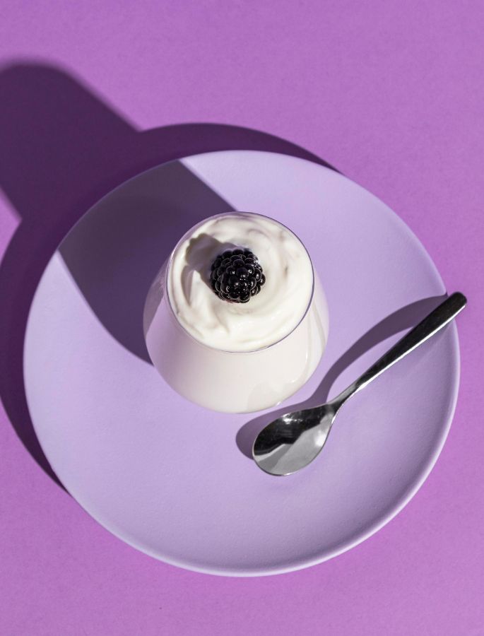 Creamy dessert like panna cotta with blackberry on purple plate and spoon, contrasted lighting and colorful background.