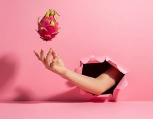 Hand emerging from pink background tossing a dragon fruit in the air, minimalist style with vivid colors and visual contrast