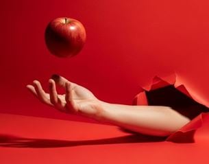 Hand emerging from torn red background tossing a red apple in the air, minimalist composition with shadow and tone on tone