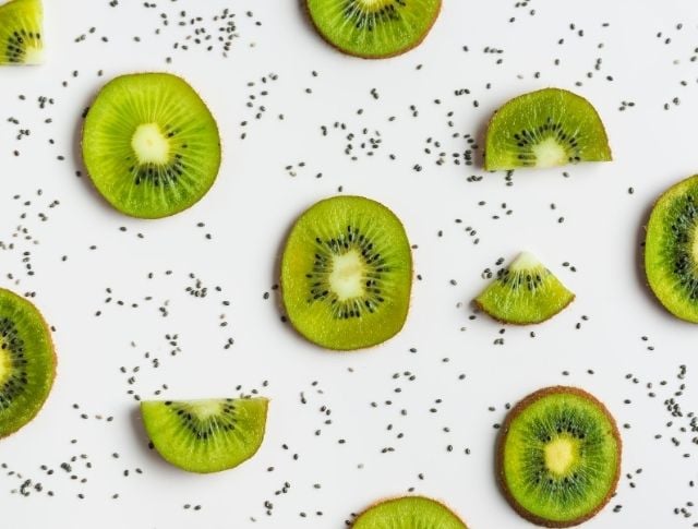 Kiwi slices arranged on white background with scattered chia seeds, minimalist graphic composition with repeating patterns