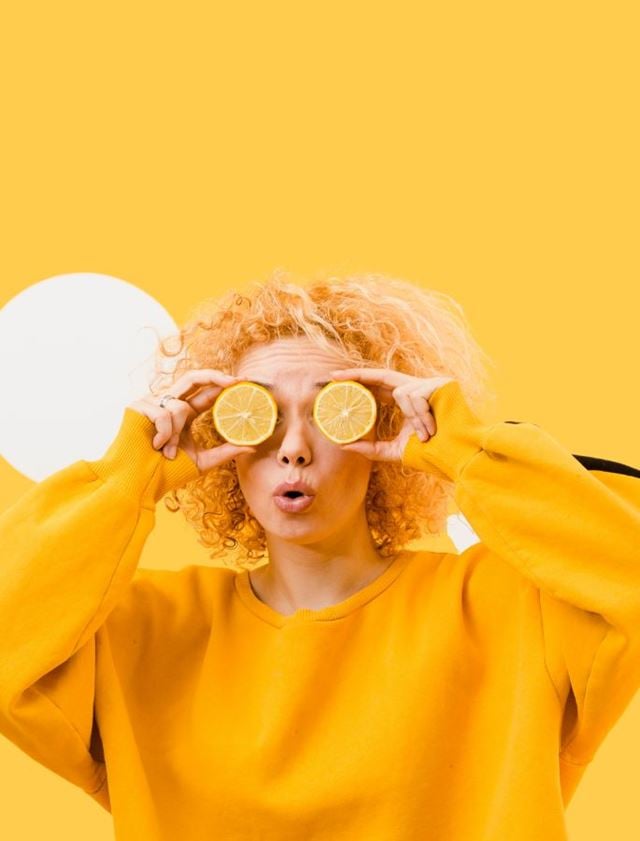 Person holding lemon slices over eyes on a yellow background, fun vitamin lifestyle summer concept