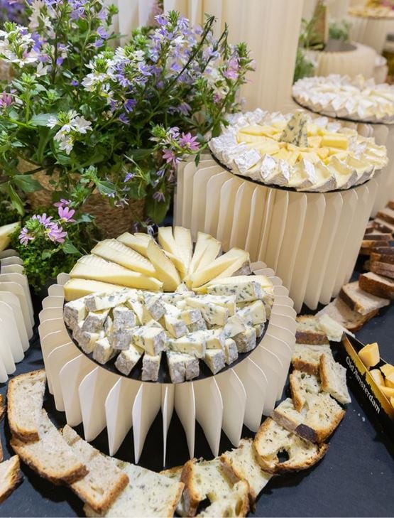 Buffet of assorted cheeses on trays, served with sliced breads and decorative purple flowers.