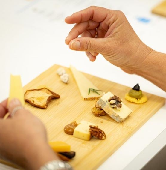 Hand arranging a tasting board with cheeses, nuts, toast and small appetizer bites.