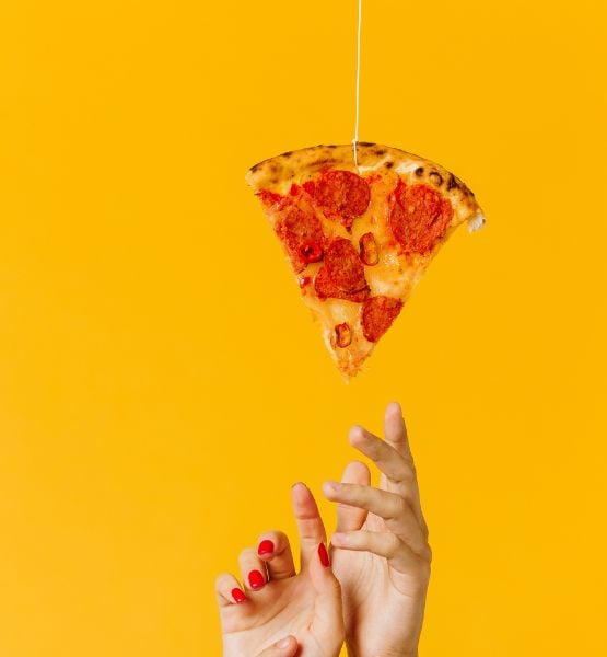 Pepperoni pizza slice hanging by string above a hand on bright yellow minimal background