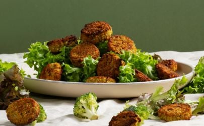 Plate of golden falafels with fresh green vegetables on an olive green background.