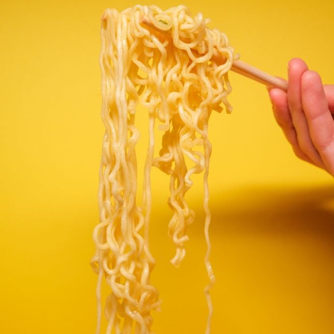 Instant noodles lifted with chopsticks against a bright yellow background.