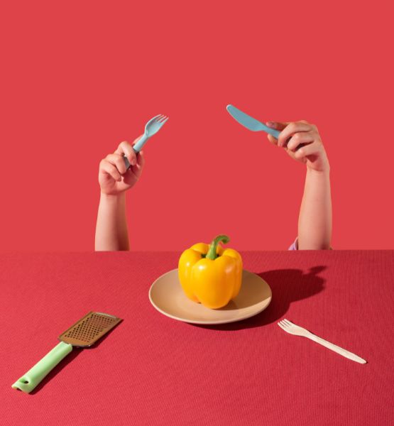 Hands holding cutlery facing a yellow pepper on a plate