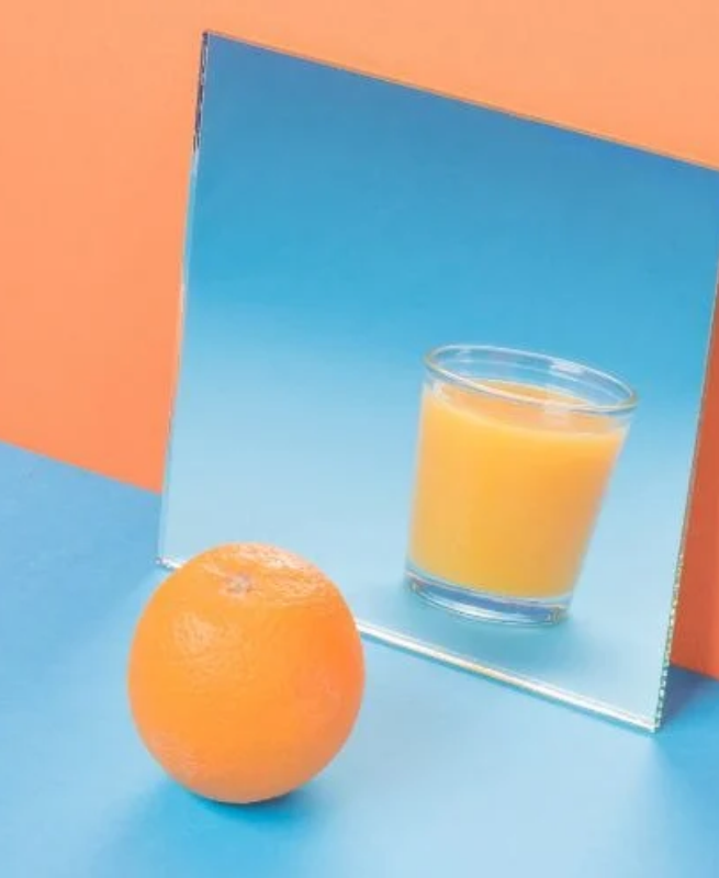 Orange in front of a mirror showing a glass of orange juice, against a blue and orange background.
