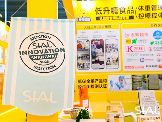 Bannière « SIAL Innovation Shanghai 2025 Selection » suspendue sur un stand d’exposition jaune, avec des panneaux d’information et des supports promotionnels lors d’un salon professionnel.