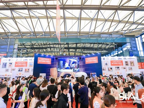 Grande scène « TuttoPizza International by SIAL » lors d’un salon professionnel, avec démonstration culinaire sur écran géant et foule de visiteurs rassemblés devant le stand dans un hall d’exposition lumineux.